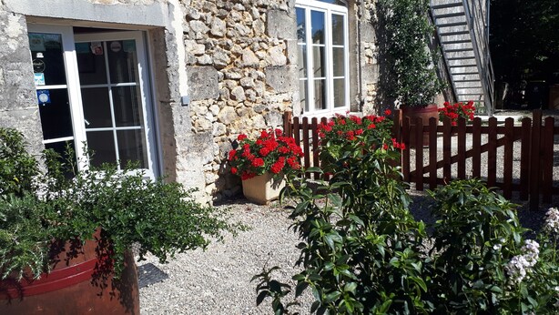 A stone building with a wooden fence, a gravel pathway, and potted plants. - Gîte Domaine de La Gravette (Cubnezais)