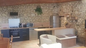 A compact kitchen with a stone wall, a microwave, a stove, a refrigerator, and a television. - Gîte Domaine de La Gravette (Cubnezais)