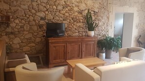 A stone-walled room with a wooden cabinet, a television, two white sofas, and a large potted plant. - Gîte Domaine de La Gravette (Cubnezais)