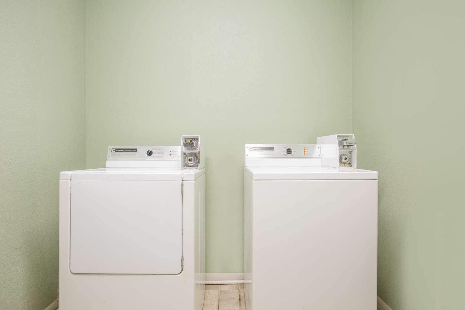 Two white front-loading washing machines in a corner with light green walls.