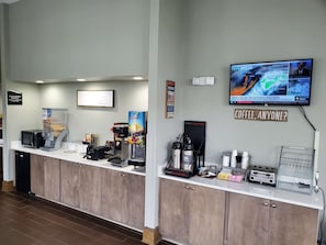 A coffee station with a TV displaying a weather forecast, a sign reading 'Coffee, Anyone?', and a microwave. - Surestay Hotel by Best Western North Myrtle Beach (North Myrtle Beach)