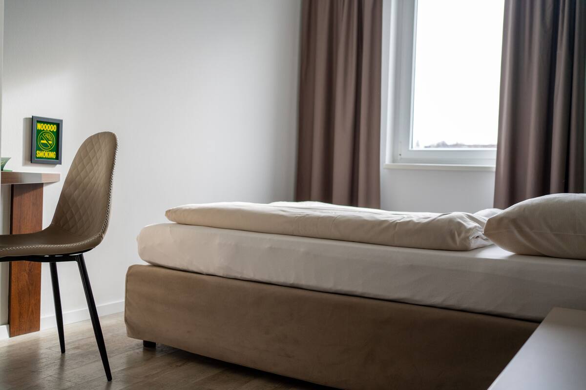 A bedroom with a bed, a chair, a desk, and a window with curtains.