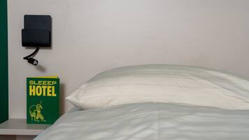 A bed with white bedding, a green sign with 'SLEEP HOTEL' text, and a black object on the wall.