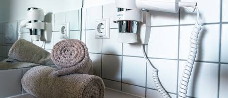 A bathroom with a towel rack holding two rolled towels, a hairdryer, and a wall-mounted power outlet.
