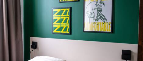 Un dormitorio con pared verde, una cama con ropa de cama blanca y tres carteles enmarcados.