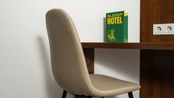 A chair with a high backrest and a cushion, positioned next to a wooden table. On the table, there is a green book titled "SLEEP HOTEL" with a yellow and white illustration on the cover.