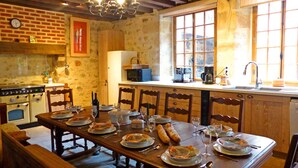 Une cuisine rustique avec des meubles en bois, une table à manger pour quatre personnes et une grande fenêtre laissant entrer la lumière naturelle.