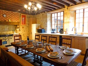 Una cuina rústica amb armaris de fusta, una taula de dinar per a quatre persones i un gran finestral que deixa entrar llum natural.
