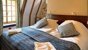 A bedroom with a wooden headboard, a large window with curtains, a bed with patterned bedding, and a wall with a floral pattern.