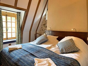 A bedroom with a wooden headboard, a large window with curtains, a bed with patterned bedding, and a wall with a floral pattern.