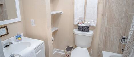A bathroom with a toilet, sink, and shower. There are white towels hanging on the wall, a small step stool, and a bottle of hand soap on the sink.