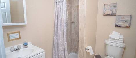A bathroom with a shower, toilet, sink, and mirror.