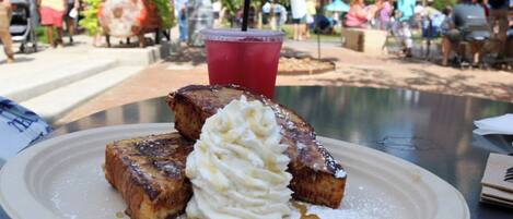 A plate of French toast with whipped cream and syrup on a table in an outdoor setting.