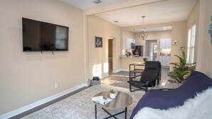 A living room with a flat-screen TV, a sofa, a coffee table, and a dining area in the background. - 3br/2ba Remodeled House Near Downtown (San Antonio)