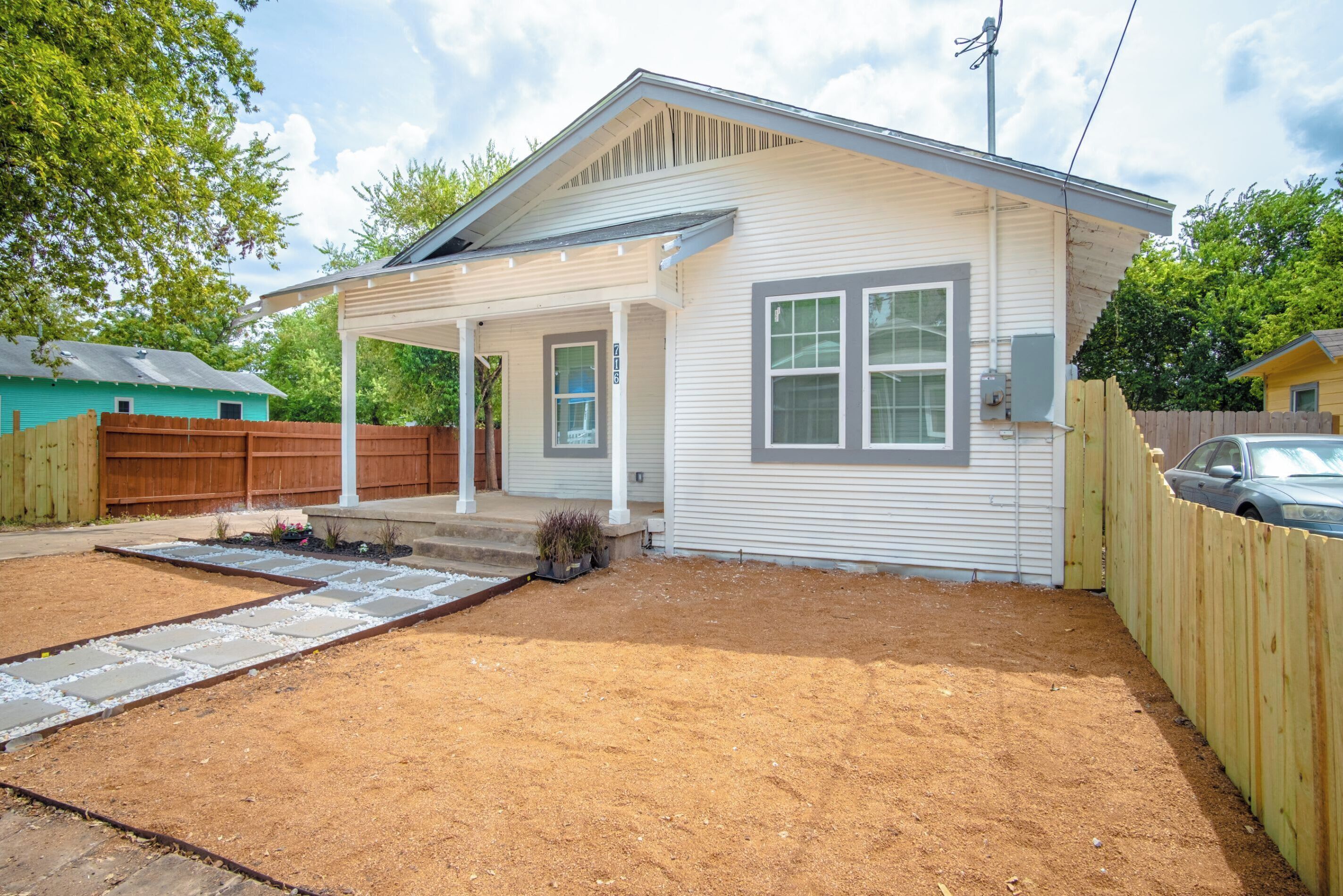 A single-story house with a covered porch, a fenced yard, and a gravel driveway.