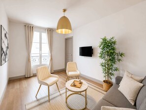 A modern living room with a sofa, two armchairs, a coffee table, a television, and a potted plant.