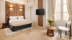 Ein modernes Schlafzimmer mit Bett, Nachttischen, Fernseher, Sessel und einem Fenster mit Vorhängen.