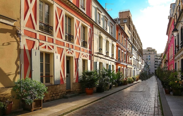A cobblestone street lined with colorful buildings, potted plants, and balconies.