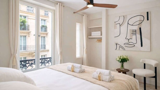 Ein Hotelzimmer mit Bett, Deckenventilator, Blick auf den Außenbalkon und einer Wand mit abstrakter Kunst.