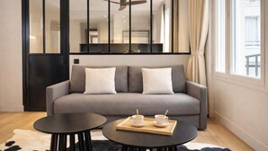 A modern living room with a grey sofa, two black round tables, a cowhide rug, and a large window with curtains. - Champs-Elysées - Prestige flat with lift Matignon (Paris)