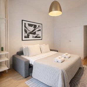 A modern bedroom with a bed, pillows, a framed abstract artwork, a hanging pendant light, and a wardrobe.