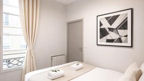 A hotel room with a bed, a ceiling fan, a radiator, a door, and a window with curtains. - Champs-Elysees stunning family flat (Paris)