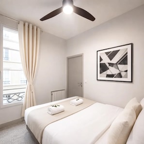 Una habitación de hotel con cama, ventilador de techo, radiador, puerta y ventana con cortinas.