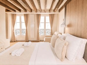A hotel room with a large bed, wooden beams, a balcony, and a view of the city.