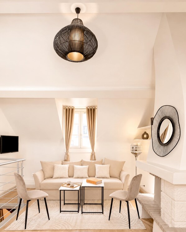 A modern living room with a sofa, two chairs, a coffee table, a TV, a fireplace, and a decorative mirror.