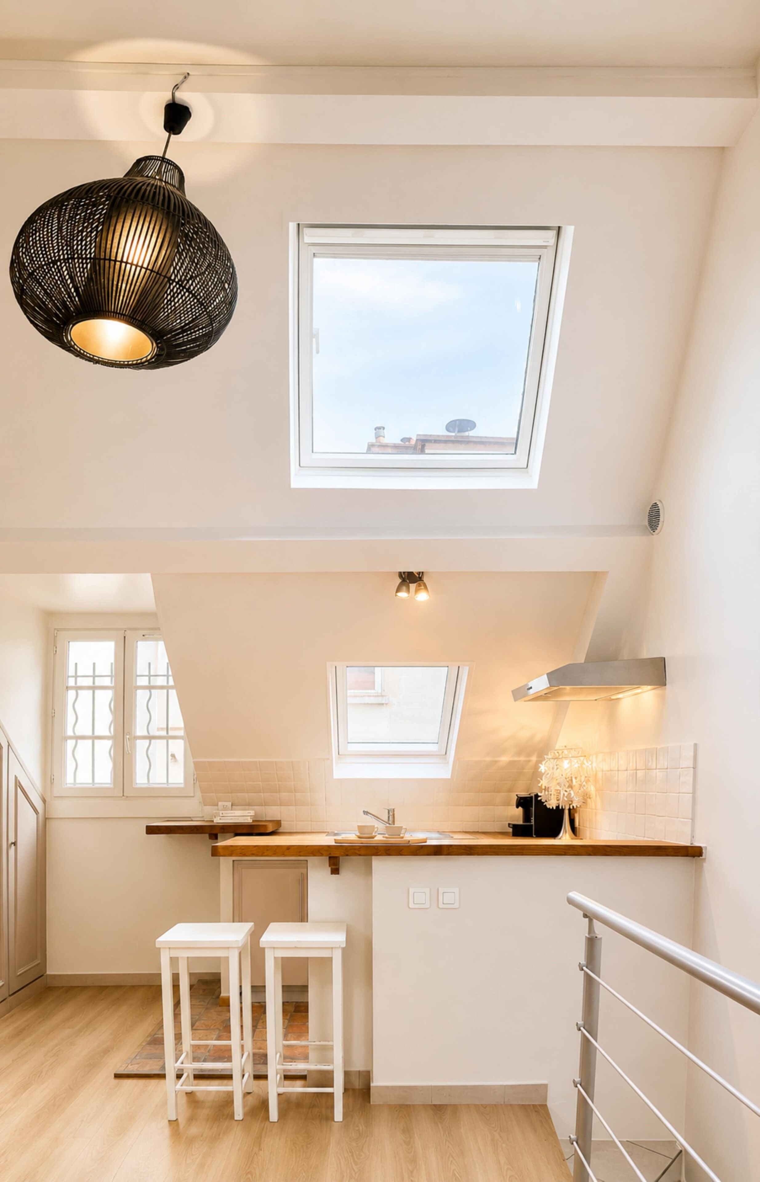 A modern kitchen with a skylight, white bar stools, and a hanging light fixture.