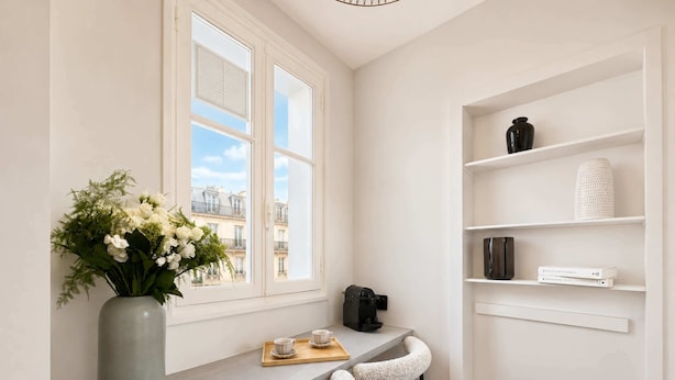 A modern kitchen with a window, a vase with flowers, a coffee machine, and bar stools.