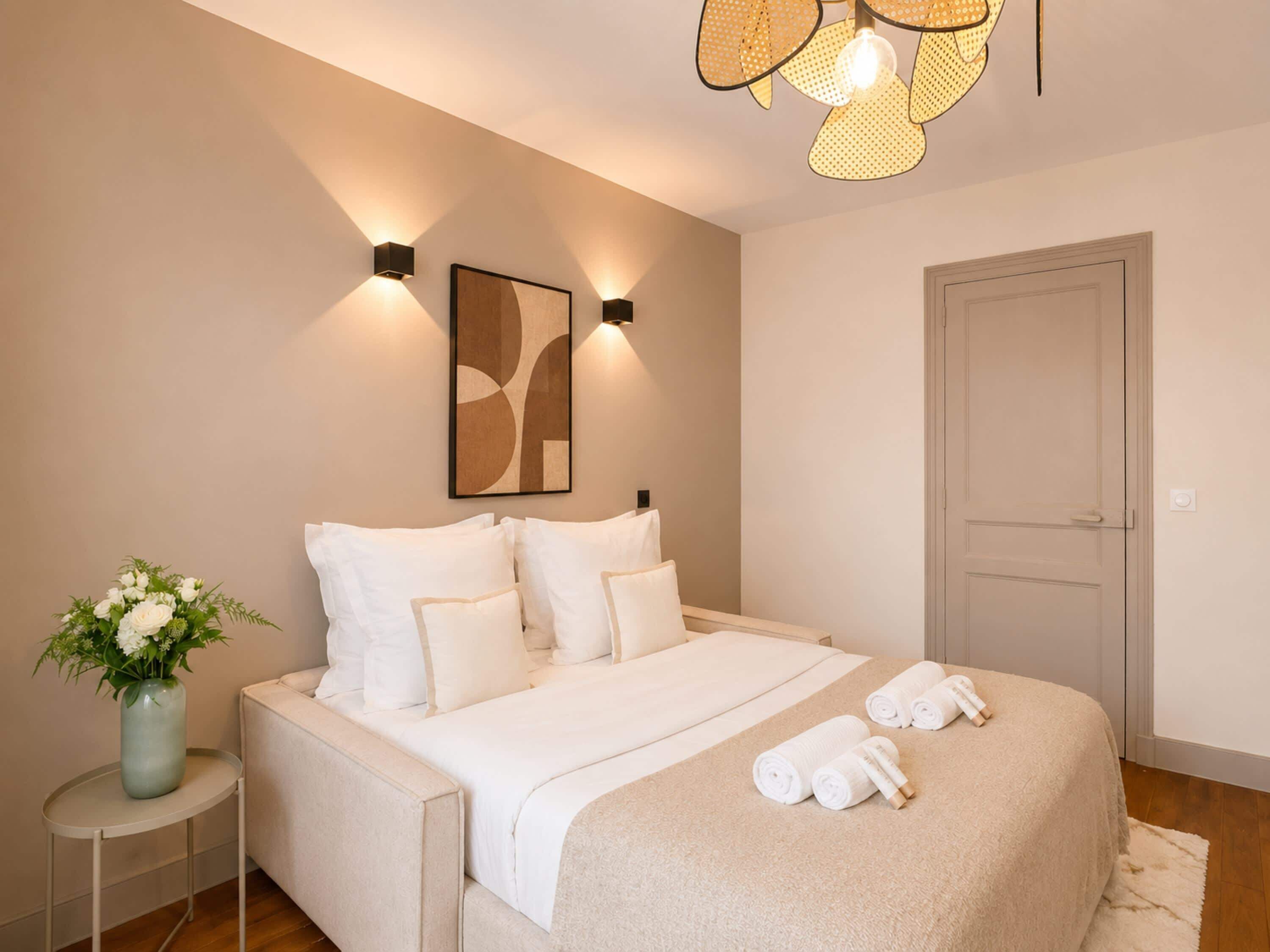 Ein Schlafzimmer mit einem Bett, Kissen, einer Blumenvase und einer Tür.