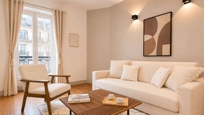 Ein modernes Wohnzimmer mit einer Couch, einem Holztisch, einem Sessel und Blick auf Gebäude durch ein Fenster.