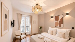 Ein Hotelzimmer mit Bett, Sessel, Schreibtisch, einem Fenster mit Vorhängen, einem Wand-Fernseher und einer Deckenleuchte.