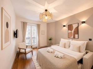Et hotelværelse med seng, stol, skrivebord, et vindue med gardiner, et TV ophængt på væggen og en loftlampe.