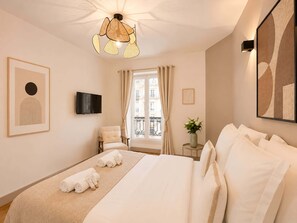 Et hotelværelse med seng, fjernsyn, et vindue med gardiner, et billede på væggen og en lampe i loftet.