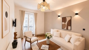 A modern living room with a white sofa, a wooden coffee table, a white armchair, a framed picture, and a decorative vase.