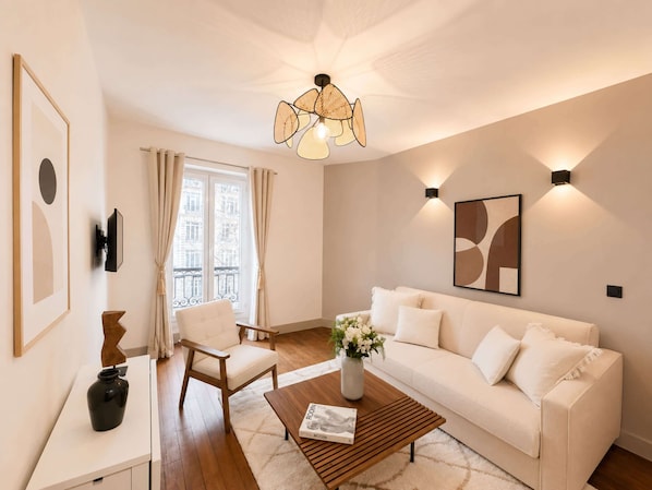 A modern living room with a white sofa, a wooden coffee table, a white armchair, a framed picture, and a decorative vase. - Arc de Triomphe stunning property with lift (Paris)
