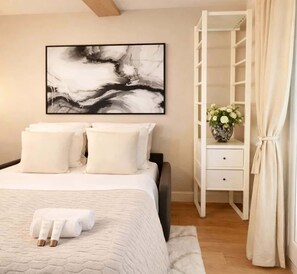 A neatly arranged bedroom with a bed, a bedside table with a vase of flowers, a wardrobe, and a large abstract painting on the wall. - Splendid apartment - Notre Dame Cathedral (Paris)
