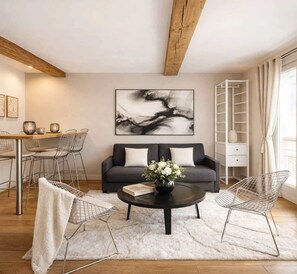 A modern living room with a sofa, coffee table, and wire chairs. There is a painting on the wall and a white cabinet with a ladder. - Splendid apartment - Notre Dame Cathedral (Paris)