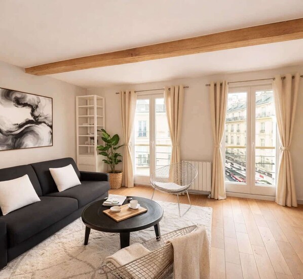 A modern living room with a black sofa, a round coffee table, a white chair, and a large window with curtains. - Splendid apartment - Notre Dame Cathedral (Paris)