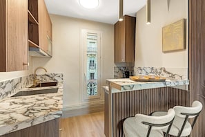 A modern kitchen with marble countertops, wooden cabinets, a built-in island with bar stools, and a view of a balcony. - Eiffel Tower - Best deal (Paris)
