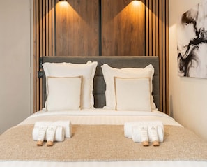 A neatly made bed with pillows and towels, a bedside table with a remote control, and a wall-mounted light fixture.