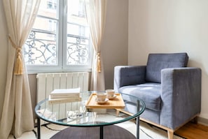 A room with a glass table, a grey sofa, and a window with curtains.