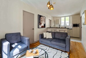 Un salon moderne avec un canapé gris, un fauteuil bleu et une table basse sur laquelle se trouvent des tasses et des soucoupes.
