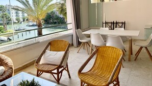 Ein modernes Zimmer mit Balkon, Korbstühlen, einem Esstisch und Blick auf einen Jachthafen.