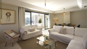Ein modernes Wohnzimmer mit weißen Sofas, einem Glastisch und einem Korbstuhl.