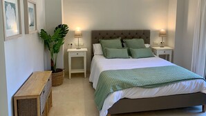 Ein ordentlich eingerichtetes Schlafzimmer mit einem großen Bett, zwei Nachttischen, einer Hängelampe und einer Topfpflanze.