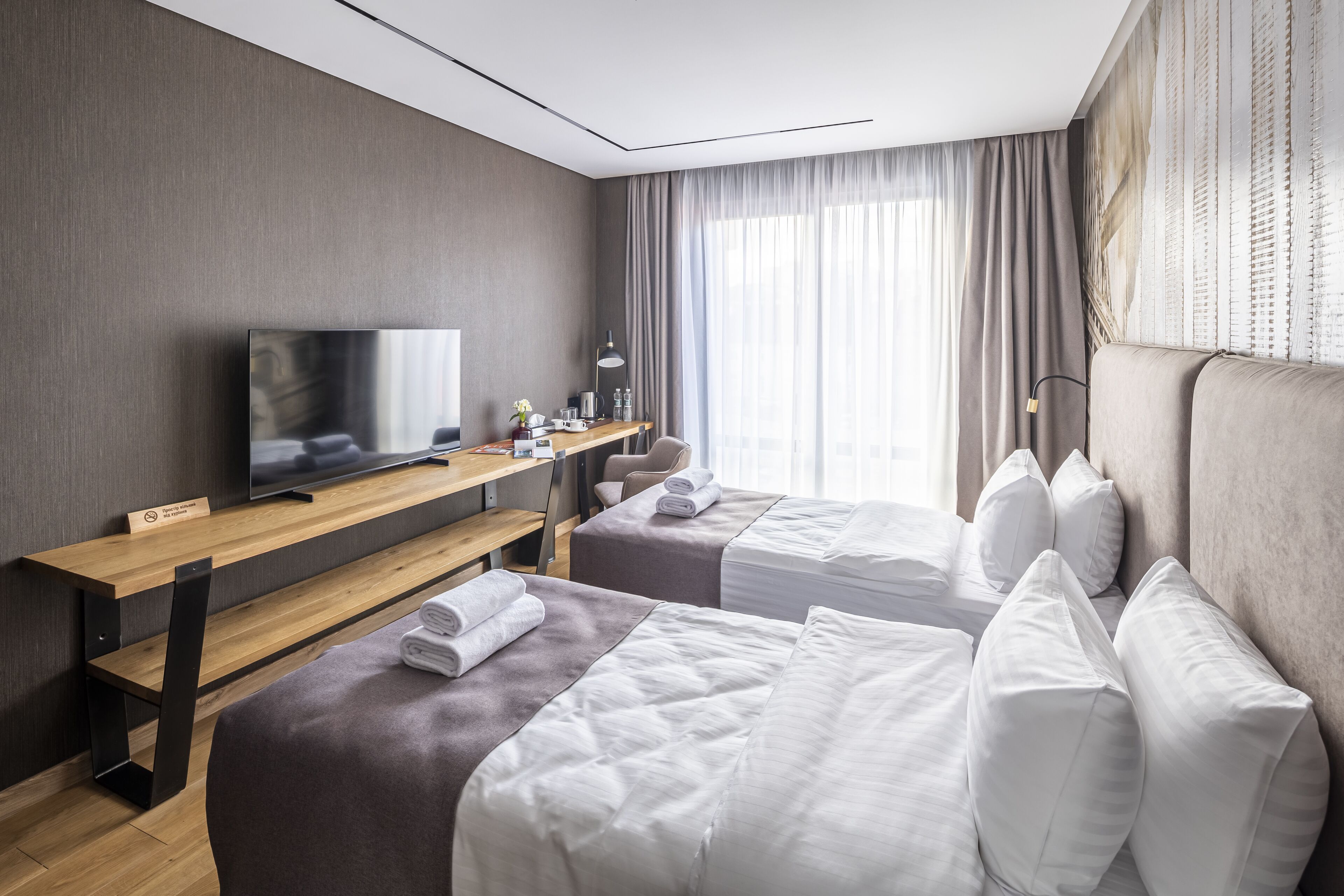 Une chambre d’hôtel avec deux lits, un bureau avec une télévision et une fenêtre avec des rideaux.