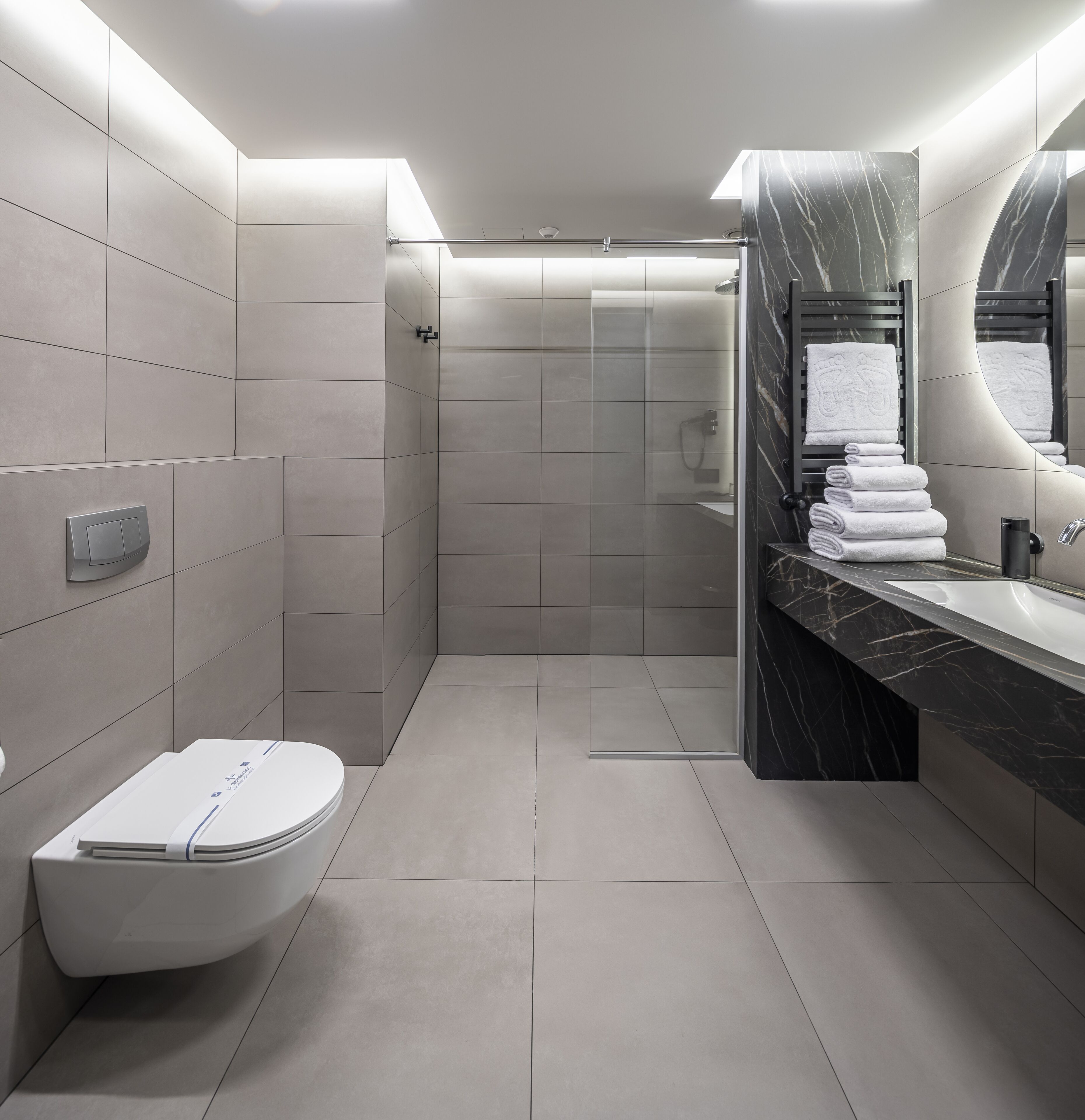 Et moderne badeværelse med toilet, brusebad og et håndvaskarrangement med marmorbordplade.